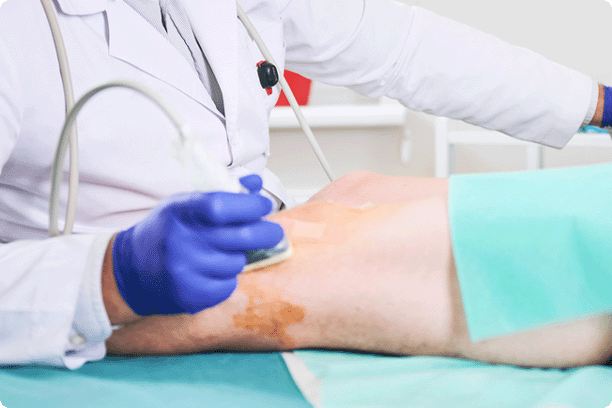 Doctor making ultrasound diagnostics, patient lying on couchette. Male specialist wearing uniform and glasses, looking at screen.