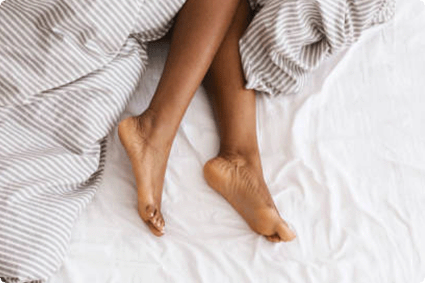 Slim, perfect and beautiful crossed woman legs on bed at vacation and holiday. Cropped of erotically lying on bed african american lady in bedroom and crumpled white bed clothes, top view, empty space